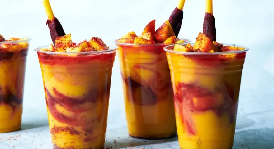 Färgglada mangodrycker med chili och fruktbitar. En perfekt guide för como hacer mangoneadas!
