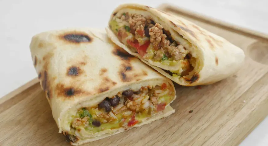 Två halverade burritos de carne med köttfärs, bönor, ris och grönsaker på en träskärbräda.