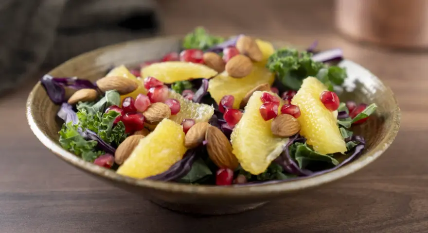 En färgstark sallad med apelsinklyftor, granatäppelkärnor, mandlar och olika typer av lechuga som grönkål och rödkål.