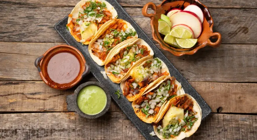 Tacos al pastor med saftig fläskkött, ananas, lök och koriander. Serveras med salsa verde, bönor och lime.