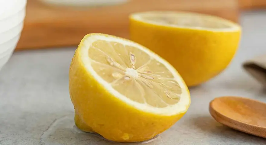 Två halvor av en saftig citron ligger på en grå yta. En träsked ligger bredvid. Perfekt för att pressa ut lite jugo de limón.