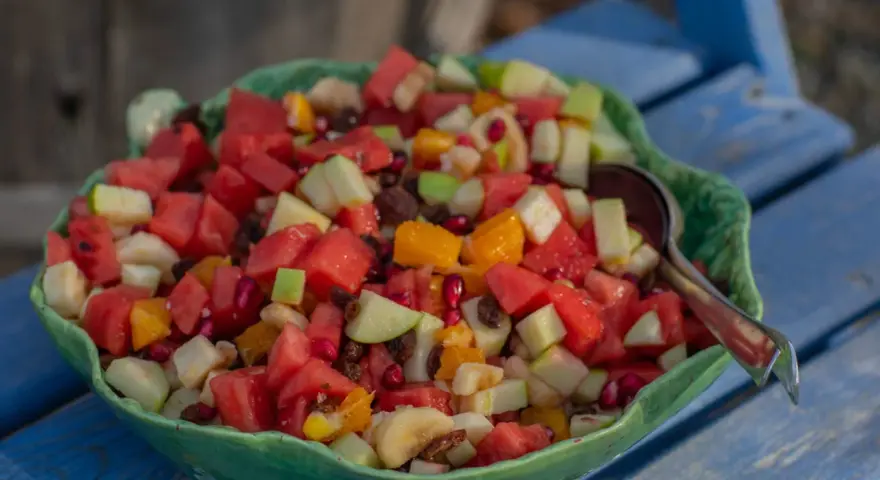 En stor skål med en färgglad ensalada de frutas, fylld med vattenmelon, äpple, apelsin, banan och granatäpple.
