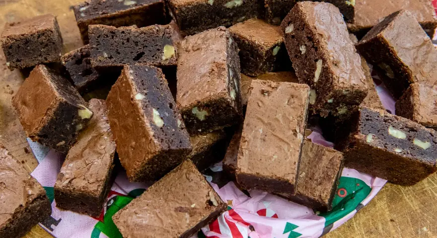 En hög med saftiga, hembakade pasteles de chocolate, vissa med nötter, ligger på ett mönstrat papper.