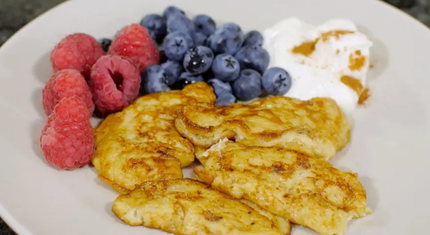 En tallrik med gyllene pannkakor, färska hallon, blåbär och en klick yoghurt med kanel. Perfekt för cenas para diabeticos.