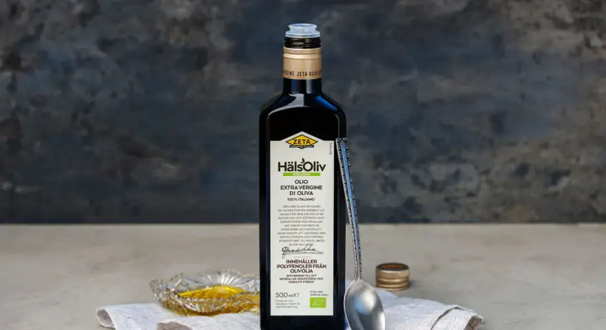 En flaska Zeta Hälsoliv Ekologisk Olio Extra Vergine di Oliva, perfekt aceite de oliva para cocinar. En sked och en liten skål med olja syns också.