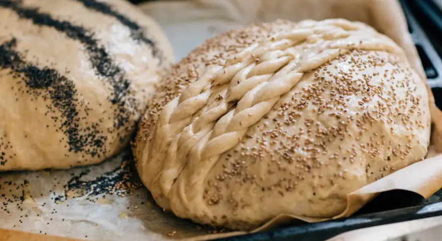 Två olika tipos de pan dulce, en med vallmofrön och en flätad med sesamfrön, redo att bakas.