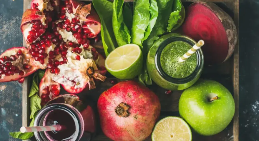 En låda med färska frukter och grönsaker, inklusive granatäpplen, äpplen, lime, rödbetor och gröna smoothies. Perfekt för naturliga botemedel mot gastrit.
