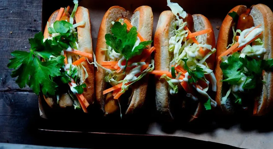 Fyra läckra korv med bröd, toppade med krispig kål, morötter och persilja. Enkel guide: como hacer un hot dog.