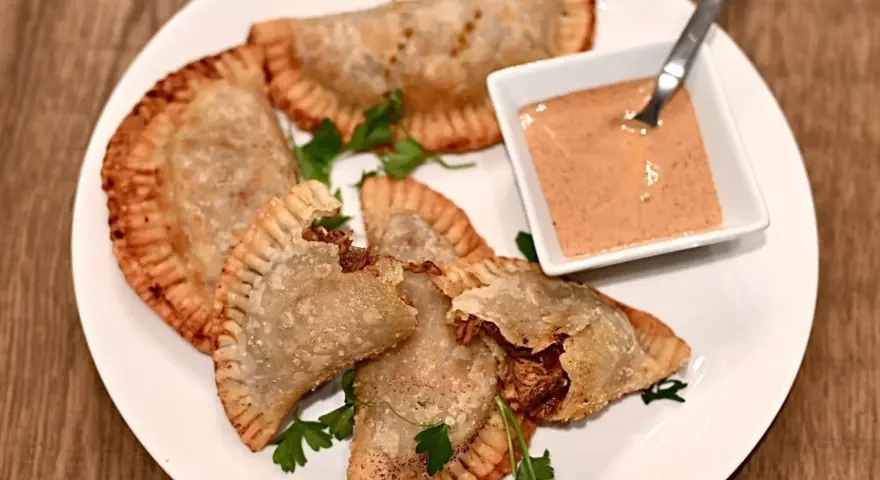 Friterade pastelitos de pollo med en krämig dippsås och persilja på en vit tallrik.