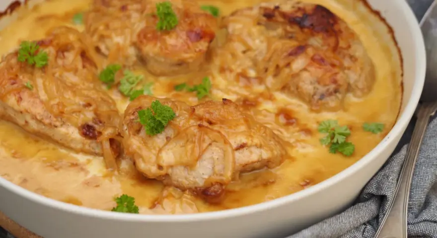 En ugnsform med saftig pollo encebollado salvadoreño, kyckling i en krämig löksås, garnerad med persilja.
