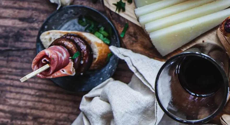 En läcker pinchos de carne med prosciutto, bröd och en skiva korv, serverad med ost och rödvin.