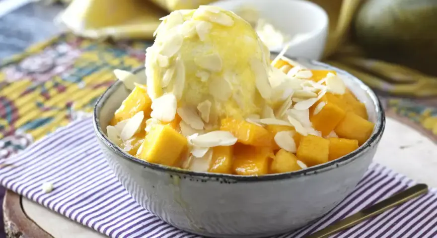 En skål med tärnad mango och en kula vaniljglass, toppad med mandelflagor. En härlig mango en miel-dessert.
