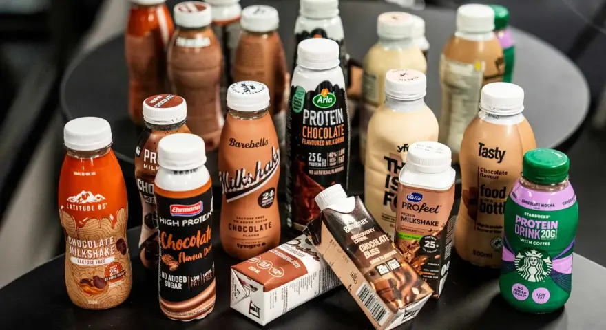 En samling flaskor och kartonger med olika sorters batido de proteinas, mestadels chokladsmak.