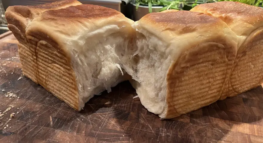 Mjukt och fluffigt **pan de leche** som brutits isär på en träskärbräda. Den gyllene skorpan kontrasterar mot det vita, trådiga inkråmet.