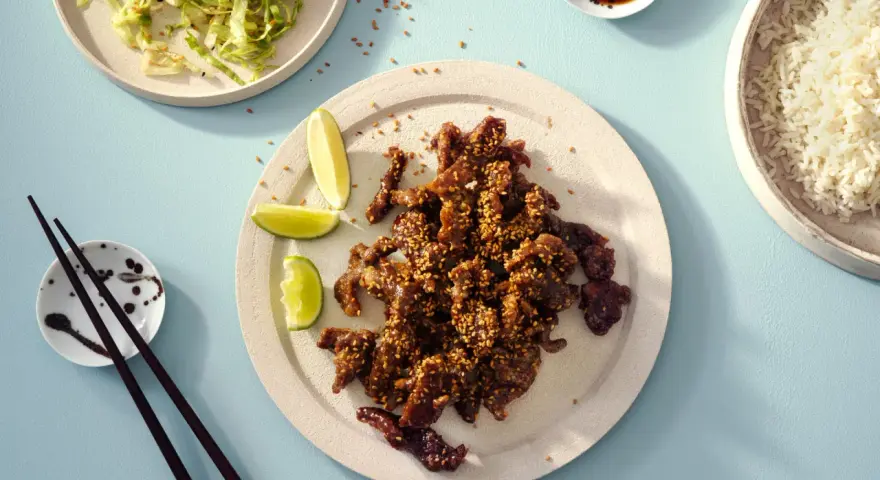 Krispiga chicharrones de cerdo med sesamfrön, serverade med ris, sallad och limeklyftor.
