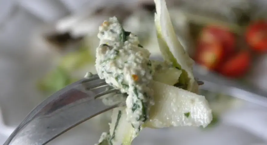 En gaffel med en krämig sallad, kanske med inslag av papayakärnor, nära körsbärstomater.
