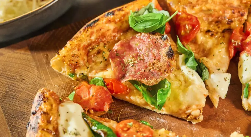 Njut av en utsökt pizza med färska **ingredientes para pizza** som salami, tomater och basilika, serverad på en träskärbräda.