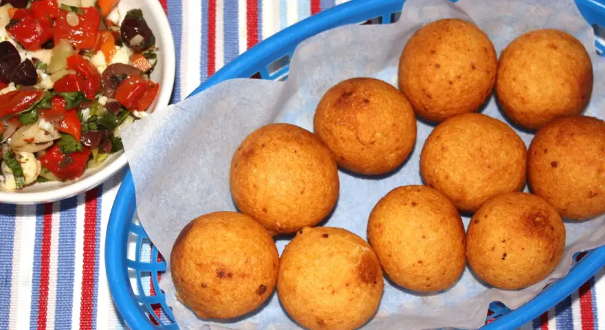 Gylla gyllenbruna friterade bollar, som visar hur man gör buñuelos, i en blå korg. Bredvid en skål med en färgglad sallad.