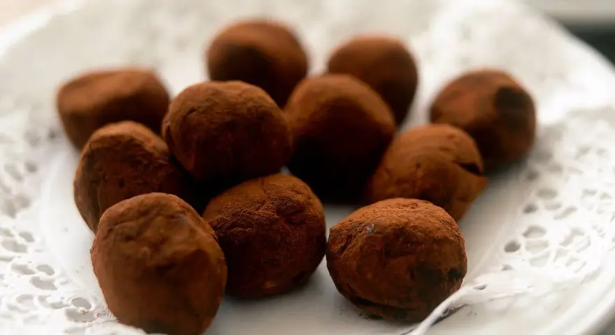En hög med chokladtryfflar, pudrade med kakao, ligger på en vit spetsduk.