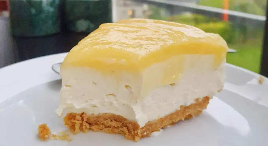 En bit krämig cheesecake med gul topping, perfekt för den som vill lära sig como hacer un cheesecake.