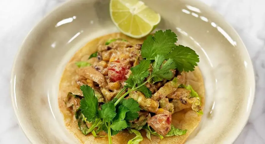 En läcker tostada de pollo med kyckling, majs, tomat och koriander, toppad med en limeklyfta.