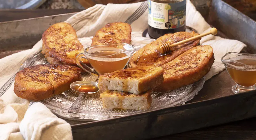 Gylla, gyllene torrejas en miel, serverade på ett fat med honung och en honungsstav.