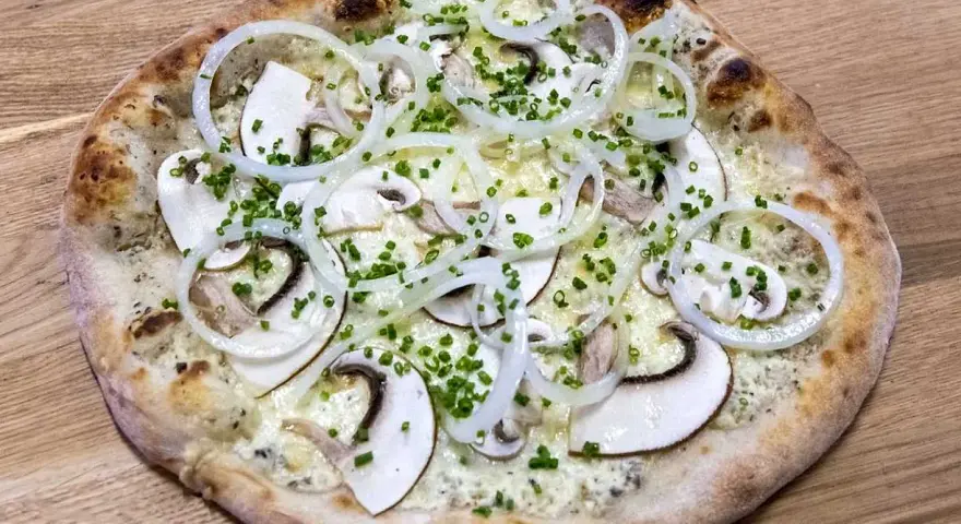 En pizza de hongos med tunna skivor champinjoner, lökringar och gräslök på en träbakgrund.