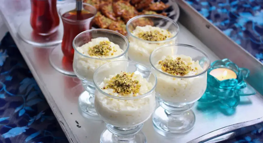 Fyra glas med krämig arroz en leche salvadoreño, toppad med pistagenötter. Två glas med te och en ljuslykta fulländar serveringen.