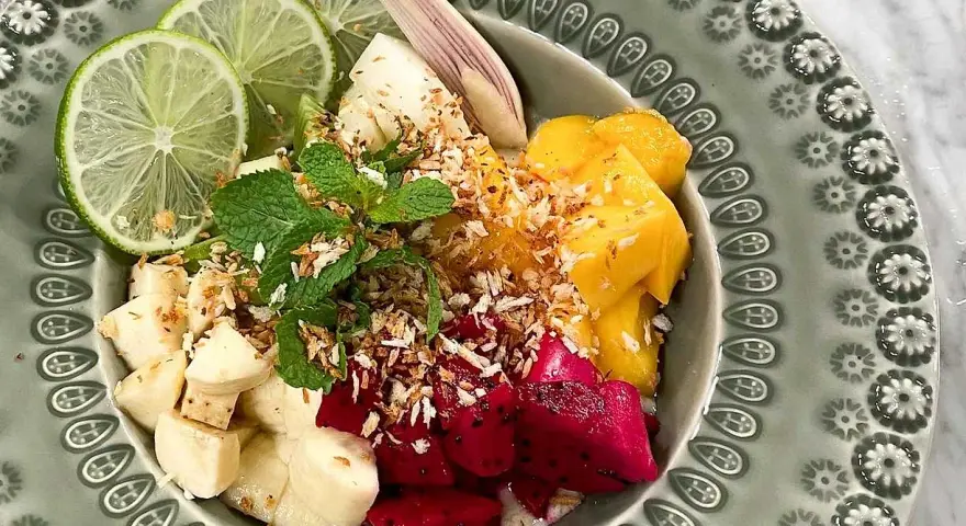 Fruktskål med mango, drakfrukt, banan, lime och mynta, toppad med rostad kokos. En härlig frukost som påminner om dulce de nance.
