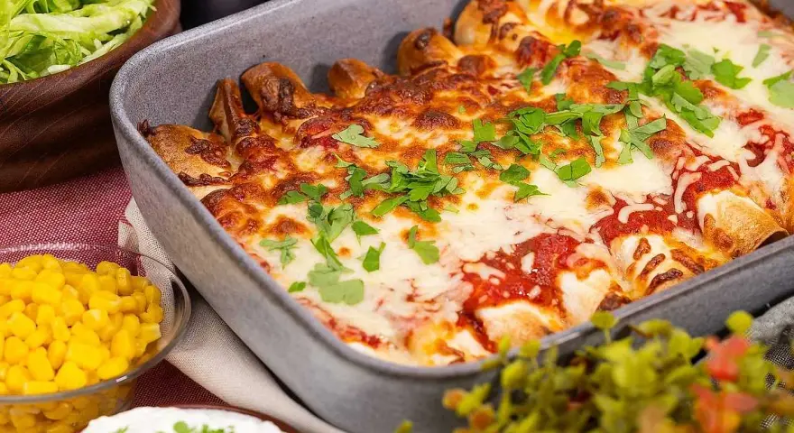 Enchiladas i ugnsform, toppade med smält ost och persilja. Tillbehör: majs, sallad och gräddfil. Perfekt för en middag med tortillas para enchiladas.