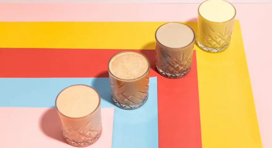 Fyra glas med olika **licuados para bajar de peso** står på en färgglad bakgrund i rött, gult, rosa och ljusblått.