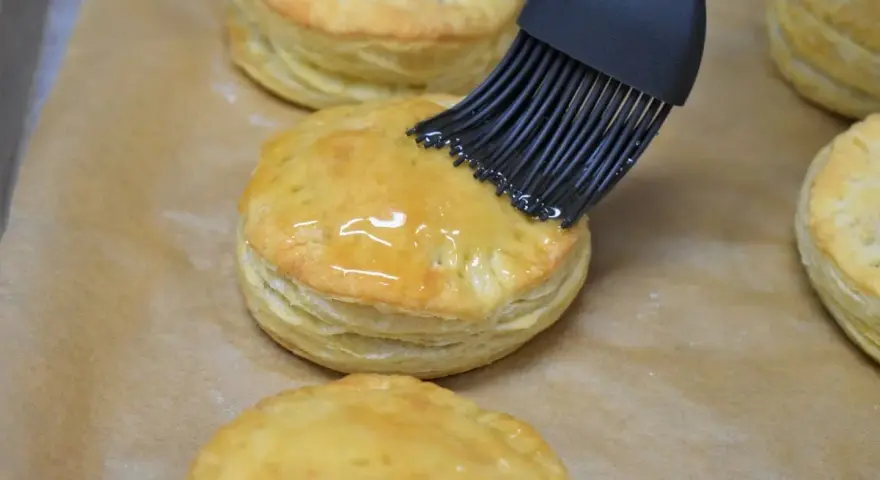 Pensel applicerar glansig glasyr på gyllene, flagnande pastelitos de carne.