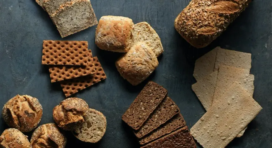 En variation av olika tipos de pan: mörkt rågbröd, knäckebröd, surdegsbröd och frallor.