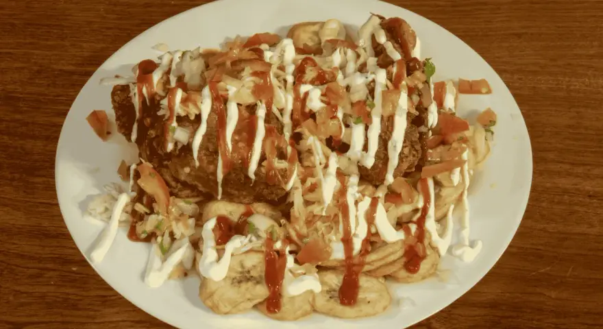 En tallrik med pollo chuco: friterad kyckling, stekta bananer, kål, tomat och majonnäs.