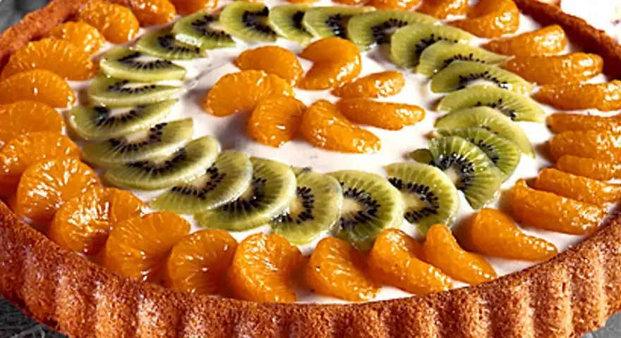 En vacker tartaleta de frutas med mandarinklyftor och kiwiskivor arrangerade i ett mönster på en krämig fyllning.