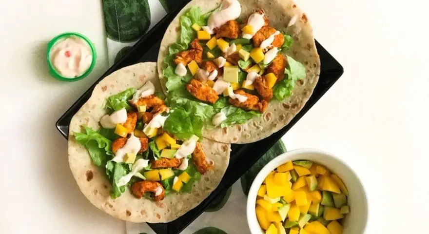 Två kycklingwraps med mango, avokado och sallad. En liten skål med mangosalsa. Hur många kalorier har en tortilla?