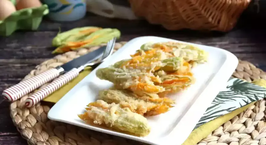 Friterade flor de calabaza på en vit tallrik, redo att avnjutas. Bredvid ligger en kniv och gaffel.