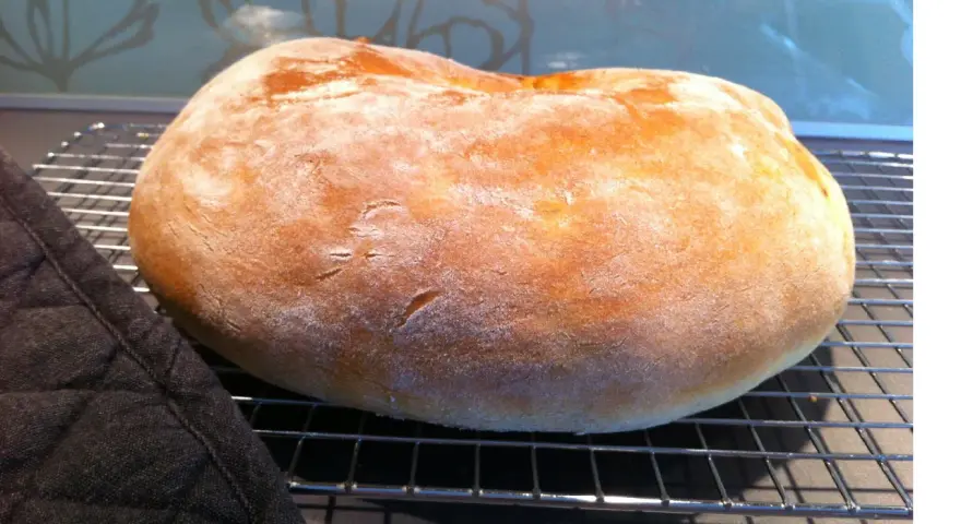 Ett nybakat, fluffigt **pan de torta** vilar på ett galler. En mörk grytlapp ligger bredvid.