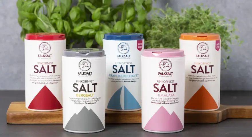 Fem olika tipos de sal från Falksalt: finkornigt, bergsalt, havssalt, Himalaya och jodberikat. Gröna örter i bakgrunden.