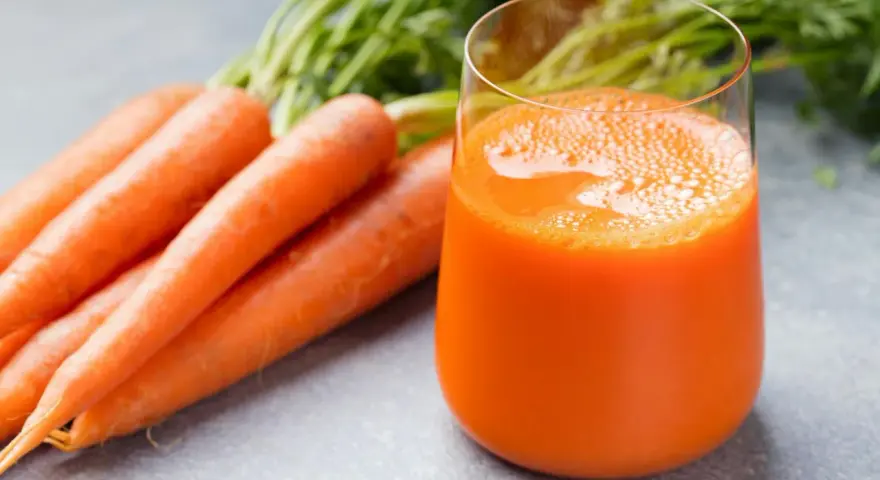 Färskt morotsjuice i ett glas, bredvid en hög med morötter. Morotsjuice är bra för synen och immunförsvaret.