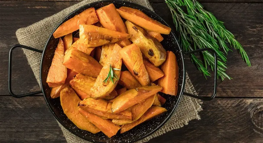 Ugnsrostad batata, eller sötpotatis, i en svart panna med rosmarin. En härlig rätt som visar vad que es batata.