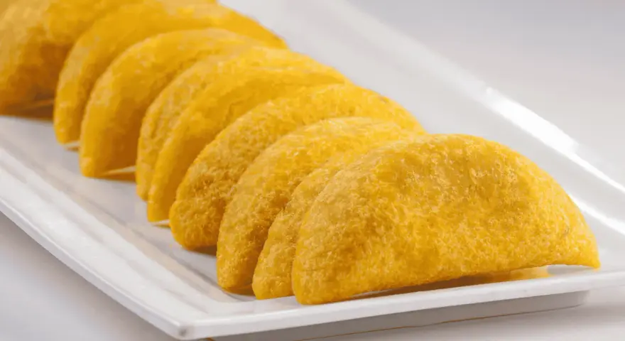 En rad gyllene empanadas de plátano ligger på en vit rektangulär bricka.