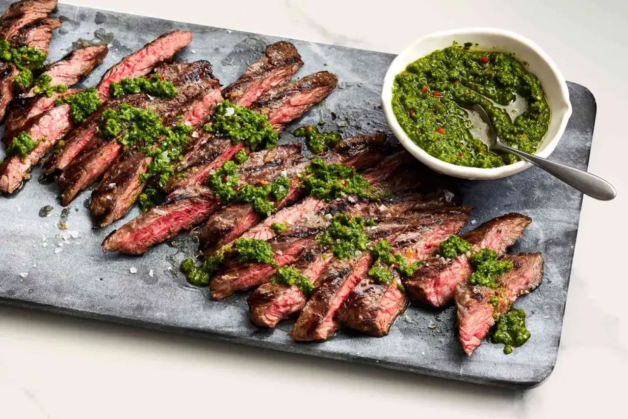 Grillad entraña de res, skivad och toppad med grön chimichurrisås, serverad på en stenplatta.
