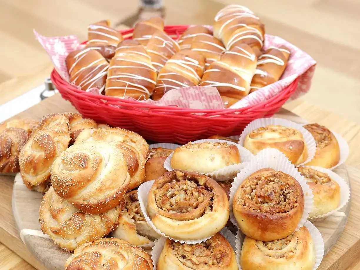 En korg med olika tipos de pan dulce, som kanelbullar och str&ouml;sselbr&ouml;d, ligger p&aring; ett tr&auml;bord.