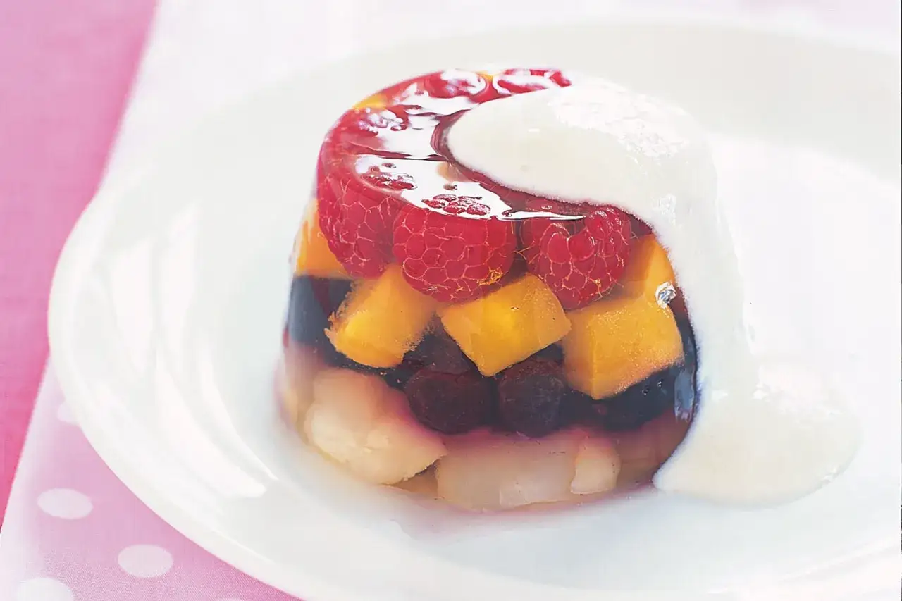 Fruktig gelatinas i glas med hallon, mango och blåbär, toppad med grädde. En härlig sommardessert.