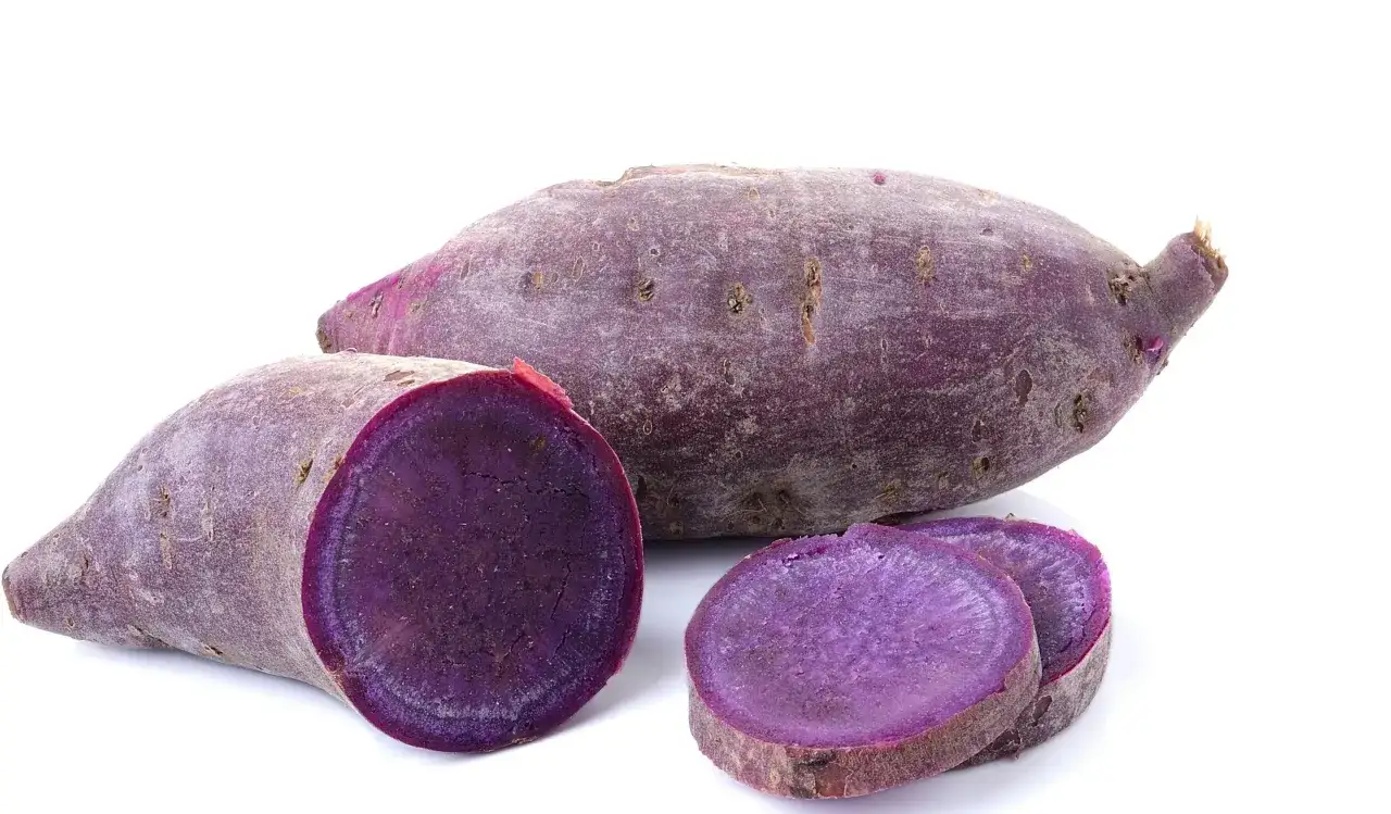 Lila batata, en sötpotatis med intensiv färg, skuren i skivor och halvor.