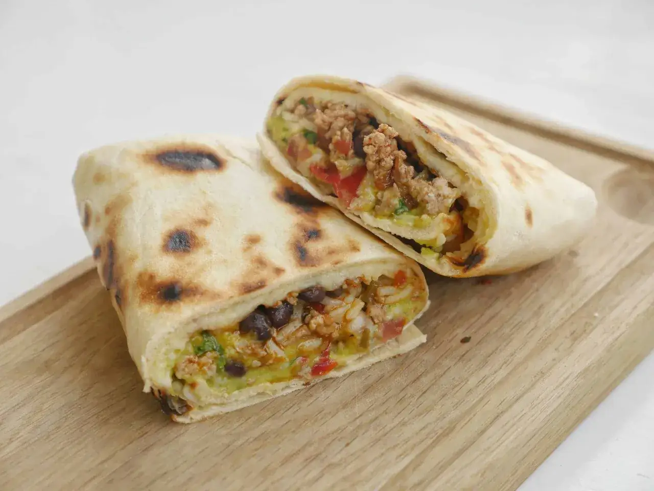 Tv&aring; halverade burritos de carne med k&ouml;ttf&auml;rs, b&ouml;nor, ris och gr&ouml;nsaker p&aring; en tr&auml;sk&auml;rbr&auml;da.