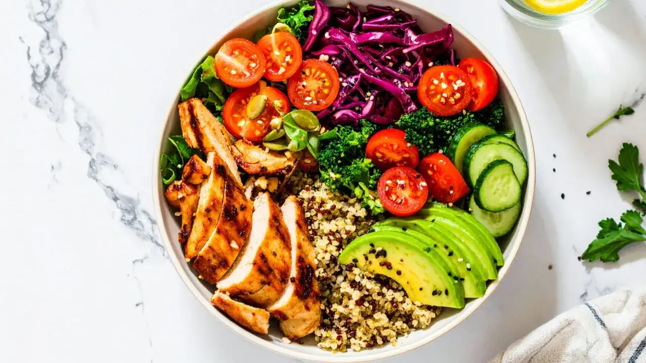 En hälsosam bowl med grillad kyckling, quinoa, avokado, tomater, gurka, broccoli och rödkål. Perfekt för att veta cuantas calorias debe consumir una persona al dia.