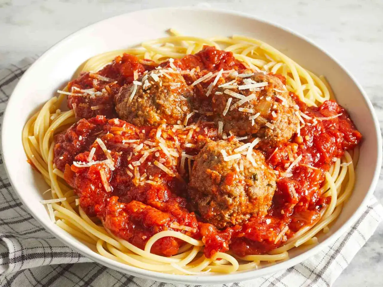 En skål med spaghetti och köttbullar i tomatsås, toppad med riven ost. Enkel guide för como hacer albondigas.