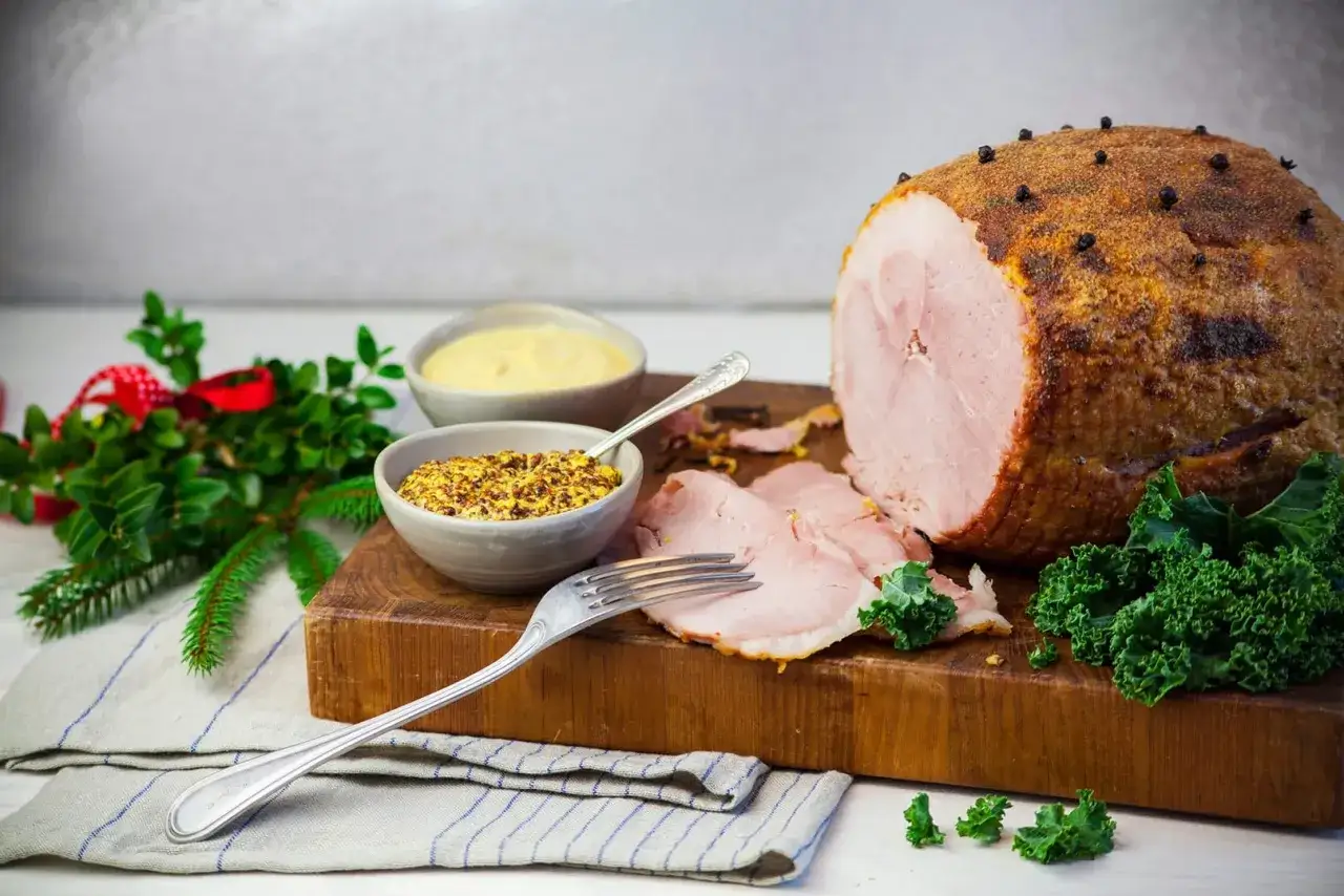 En saftig julskinka, kryddad med nejlikor, serveras med senap och grönkål. El jamón es carne de cerdo, perfekt för högtiden.
